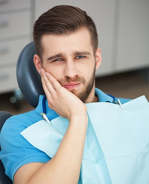 Man in need of emergency dentistry holding cheek in pain